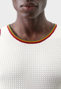 Hvit, ribbestrikket tanktop med en flerfarget stripete rund hals i rødt, grønt og gult.