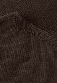 Tissu tricoté brun foncé avec un bord plié montrant des coutures détaillées et une texture sous un éclairage doux.