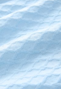 Vaaleansininen kangas, jossa on teksturoitu timanttikuvio, pehmeä neulostruktuuri ja sileä pinta. Ei näkyvää kiinnitystä tai koristeita.