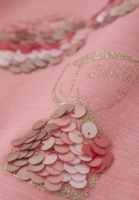 Rosa Stoff mit Paillettenverzierungen in verschiedenen Rosatönen, zusammen mit einem goldenen Glitzerumriss eines kammähnlichen Designs.