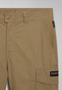 Pantaloni cargo beige realizzati in tessuto leggero. Presentano una chiusura con bottone, tasche frontali e una distintiva toppa con logo sul lato.