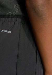 Crne atletske kratke hlače od teksturiranog materijala, s elastičnom waistband-a i vidljivim "CLIMACOOL" oznakama sa strane. Glatka površina.