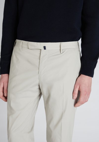 Pantalons beige clair avec une texture lisse, présentant un devant plat, des passants de ceinture et un accent bleu foncé au niveau de la taille. Coupe ajustée.