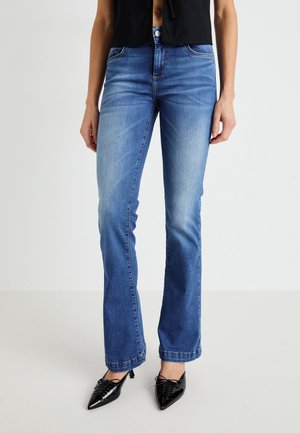 Jeans évasés en denim bleu moyen, avec une taille mi-haute, des dégradés subtils, cinq poches et des coutures contrastantes. Associés à des chaussures noires à bout pointu.