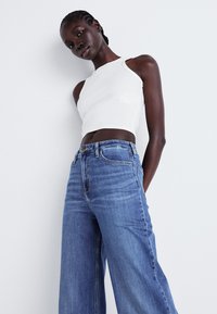 White ribbed crop top with wide shoulder straps, paired with high-waisted, light blue wide-leg jeans featuring subtle fading and five-pocket design.