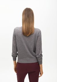 Szary dziany sweter z długimi rękawami, okrągłym dekoltem i ściągaczem na dole. Nosi się go z bordowymi spodniami. Prosty, dopasowany krój.