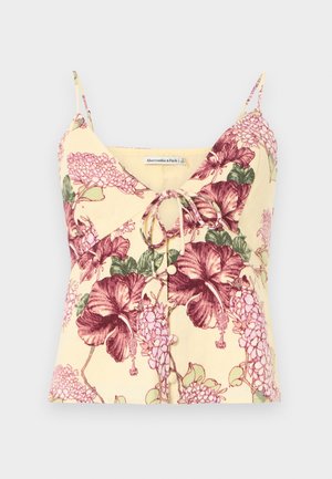 Haut jaune sans manches avec fines bretelles, imprimé floral violet, détail noué à l'avant et petits boutons au centre.