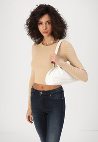 White structured handbag with curved shape and smooth texture. Model wears a beige ribbed crop sweater and dark blue fitted jeans.