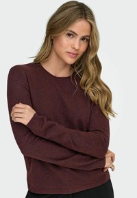 Suéter de punto burdeos con cuello redondo, mangas largas y puños acanalados. Textura suave con sutiles variaciones en el color.