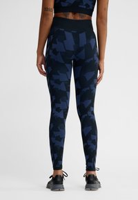 Höga leggings i marinblått med ett abstrakt geometriskt mönster. Tillverkade av stretchigt tyg, med en slät textur och en figurnära design.