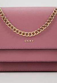 Borsa a tracolla in pelle rosa con finitura testurizzata, dotata di catene dorate e logo "DKNY" impresso sul davanti. Tre scomparti orizzontali.