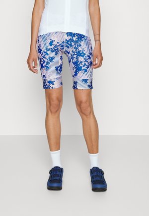 Kleurige fietsshorts met een blauw en roze bloemenpatroon, gemaakt van rekbaar materiaal, gecombineerd met blauwe fietsschoenen en witte sokken.