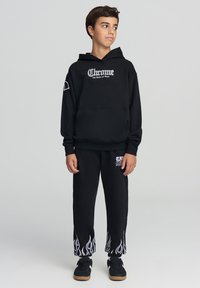 Felpa nera con logo bianco "Chrome", abbinata a pantaloni tuta neri con motivi a fiamma bianchi all'orlo. Include dettagli con tasche.