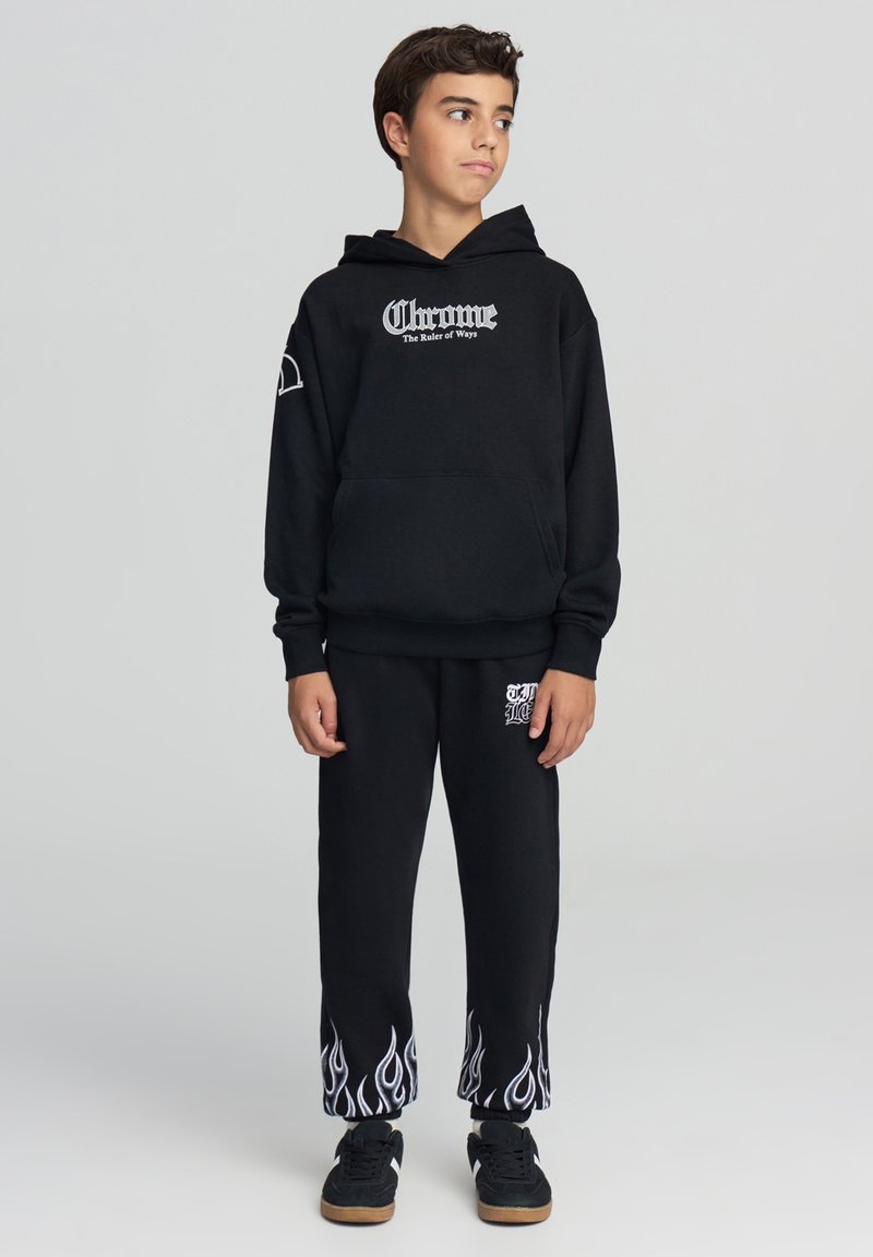 Felpa nera con logo bianco "Chrome", abbinata a pantaloni tuta neri con motivi a fiamma bianchi all'orlo. Include dettagli con tasche.
