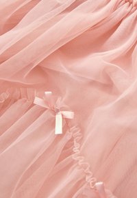 Svetloružová tylová látka so zúženými okrajmi a jemnými volánmi. Dizajn dopĺňajú dve malé saténové mašle. Mäkká a priesvitná textúra.