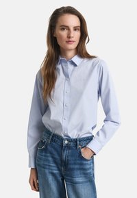 Hele sinine nööpidega särk, mis on valmistatud puuvillast, klassikalise krae ja pikkade varrukatega, koos kõrge vöökohaga siniste teksadega, millel on kulunud tekstuur.
