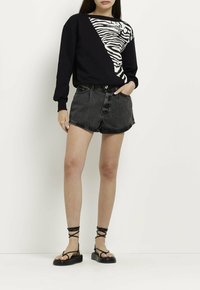Felpa nera con stampa zebra bianca su un lato, abbinata a pantaloni shorts in denim neri a vita alta e sandali neri con cinturini.