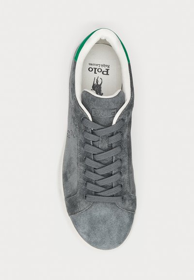 Grijze suède sneaker heeft een textuur bovenwerk, ronde neus, platte veters en een witte zool. Groene accenten op de hiel en een gemerkte binnenzool.