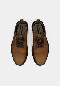 Zapatos de cuero marrón con punta redonda, suela de goma, cordones en la parte delantera y detalles de costura en tonos similares. Nombre de la marca visible en la plantilla.