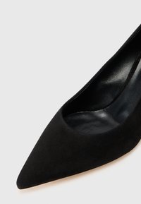 Sort ruskindspumpe med spids tå og glat finish, med lav udskæring og en tynd, tilspidset hæl for en elegant silhuet.