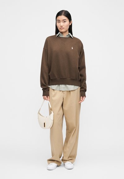 Rjava jopa, pod njo črtasta majica, bež hlače širokih nogav, bele superge in majhna bež torbica z zlatim poudarkom.