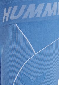Blå träningsleggings med en texturerad ribbad design. Har en vit "HUMM"-logotyp och släta detaljer i ett geometriskt mönster.