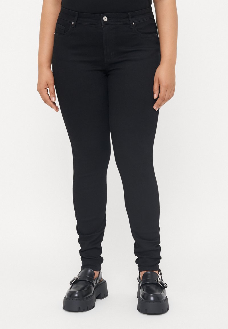 Black denim skinny jeans with a high waist, featuring front pockets, a button closure, and a smooth texture. Paired with chunky black shoes.