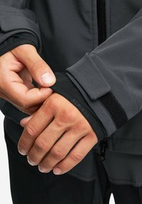 Szary rękaw kurtki z mikrofibry z czarną podszewką, z rzepem do regulacji. Widoczna jest teksturowana tkanina.