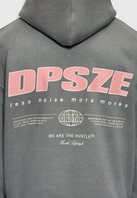 Sweat à capuche gris avec un grand texte rose "DPSZE", des phrases plus petites dont "moins de bruit plus de mouvement" et "NOUS SOMMES L'EFFORT Style de vie Effort" au dos.