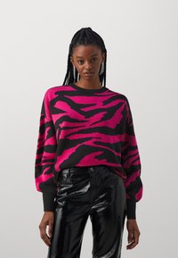 Stickad tröja med svarta och klarröda zebra-ränder, rund halsringning och ribbad fåll. Matcher med blanka svarta fusk läderbyxor.