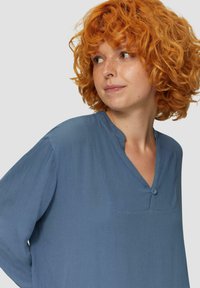 Blauwe, textuurachtige blouse met een v-hals en een enkele knoopdetail. Lange mouwen van zacht, vloeiend fabric. Licht ontspannen pasvorm.