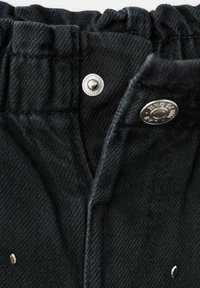 Crne traperice s nabranim pojasom, srebrnim kopčanjem na gumb i suptilnom teksturom. Vidljiva detaljna šavova.