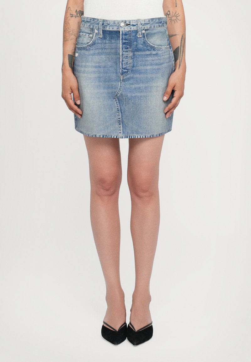 Denimkjol i ljusblått, knälång med rak skärning, fransad fåll och femficksdesign; matchad med svarta spetsiga klackskor.
