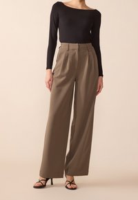 Hoge taille, wijde broek in olijfgroen stof, met plooien en een gladde textuur, gecombineerd met een aansluitende zwart blouse met lange mouwen.