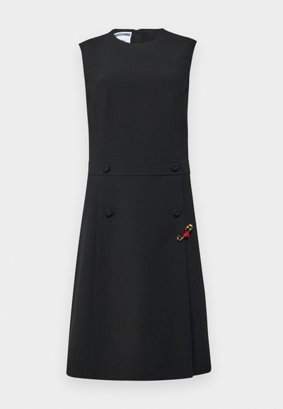 Vestido preto sem mangas com corpete ajustado, saia ampla, botões à frente e um broche dourado com detalhes vermelhos de um lado.