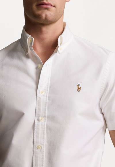 Short-sleeve white dress shirt made of cotton with a button-down collar, featuring a small embroidered brown horse logo on the chest.