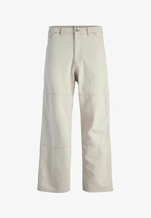 Camiseta de algodón beige con un panel horizontal blanco que muestra "ORIGINALS." Combinada con pantalones de pierna ancha beige claros y zapatillas beige.