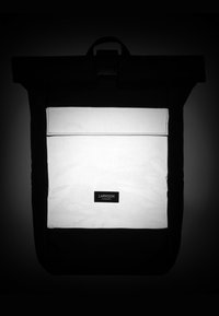 Black roll-top backpack with a white front pocket and black accents. Features a rectangular shape, adjustable straps, and a logo label.