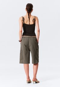 Olívazöld cargo short, puha anyagból készült. Jellemzői közé tartozik a térd hosszú szegély és két oldalsó zseb, fekete ujjatlan felsővel párosítva.