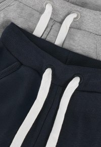 Close-up van grijze en marineblauwe sweatpants met witte trekkoorden die door ribbel-elastieken zijn geregen.