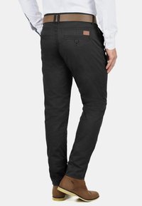 Fekete, slim fit chino nadrág, hátul bőrkiegészítővel a derékrészen, barna bokacsizmával párosítva. Simább, textúrált anyag.