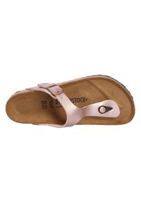 Sandalo marrone con suola piatta, caratterizzato da un fascio metallico rosa e una fibbia regolabile. All'interno si vede una soletta texturizzata e il logo del marchio.