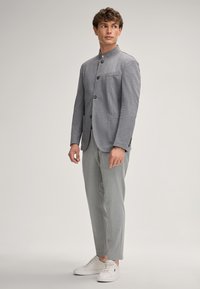 Grijze getailleerde blazer met een hoge kraag, knoopsluiting en voorzakken, gecombineerd met lichtgrijze broeken en witte sneakers.