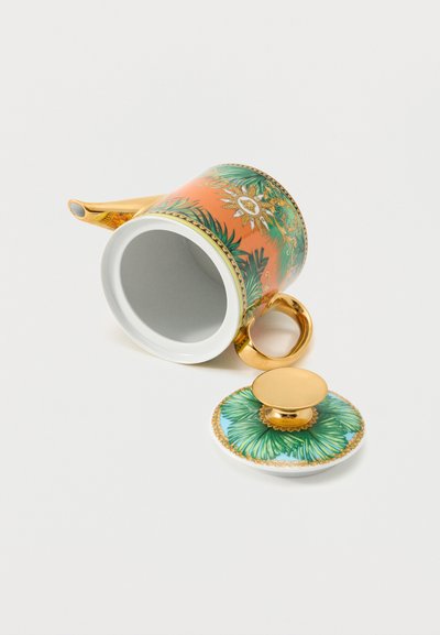 Πορσελάνινος τσαγερό με χρυσή χειρολαβή και ρύγχος, με πορτοκαλί και πράσινο τροπικό φυλλώδες σχέδιο, και αποσπώμενο καπάκι που ακουμπά δίπλα του σε λευκή επιφάνεια.