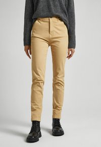 Béžové chinos vyrobené z bavlny, s přiléhavým střihem a vysokým pasem. V páru s tmavě šedým pleteným svetrem a černými šněrovacími botami.