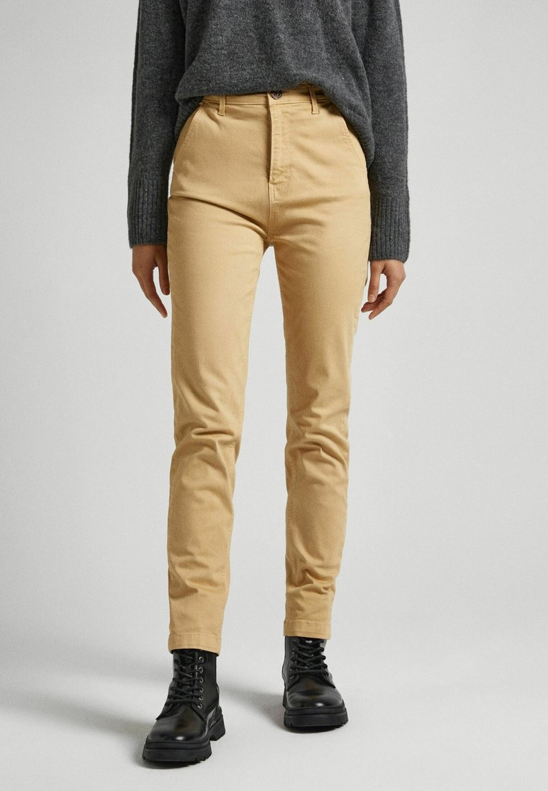 Béžové chinos vyrobené z bavlny, s přiléhavým střihem a vysokým pasem. V páru s tmavě šedým pleteným svetrem a černými šněrovacími botami.