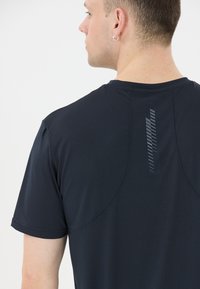 Sort atletisk t-shirt med tekstureret stof, korte ærmer og en reflekterende stribe på bagsiden for synlighed.