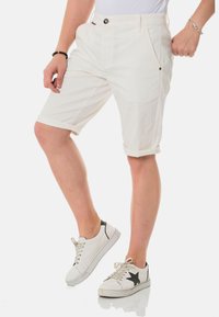Shorts en coton blancs avec un ourlet roulé, comprenant des poches latérales et une fermeture à bouton. Associés à des baskets blanches et un haut blanc uni.