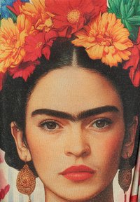 Retrato de una mujer con cabello oscuro, cejas llamativas y flores vibrantes. Lleva pendientes de oro y tiene la piel suave con labios rojos.