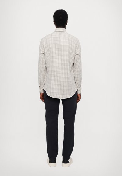 Light plaid long-sleeve shirt in beige, with a classic collar and buttoned cuffs, paired with navy pants and casual black shoes.